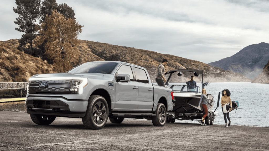 2024 Ford F-150 Lightning parked near a lake, towing a boat, highlighting its electric power and eco-friendly capabilities near Euclid, OH.