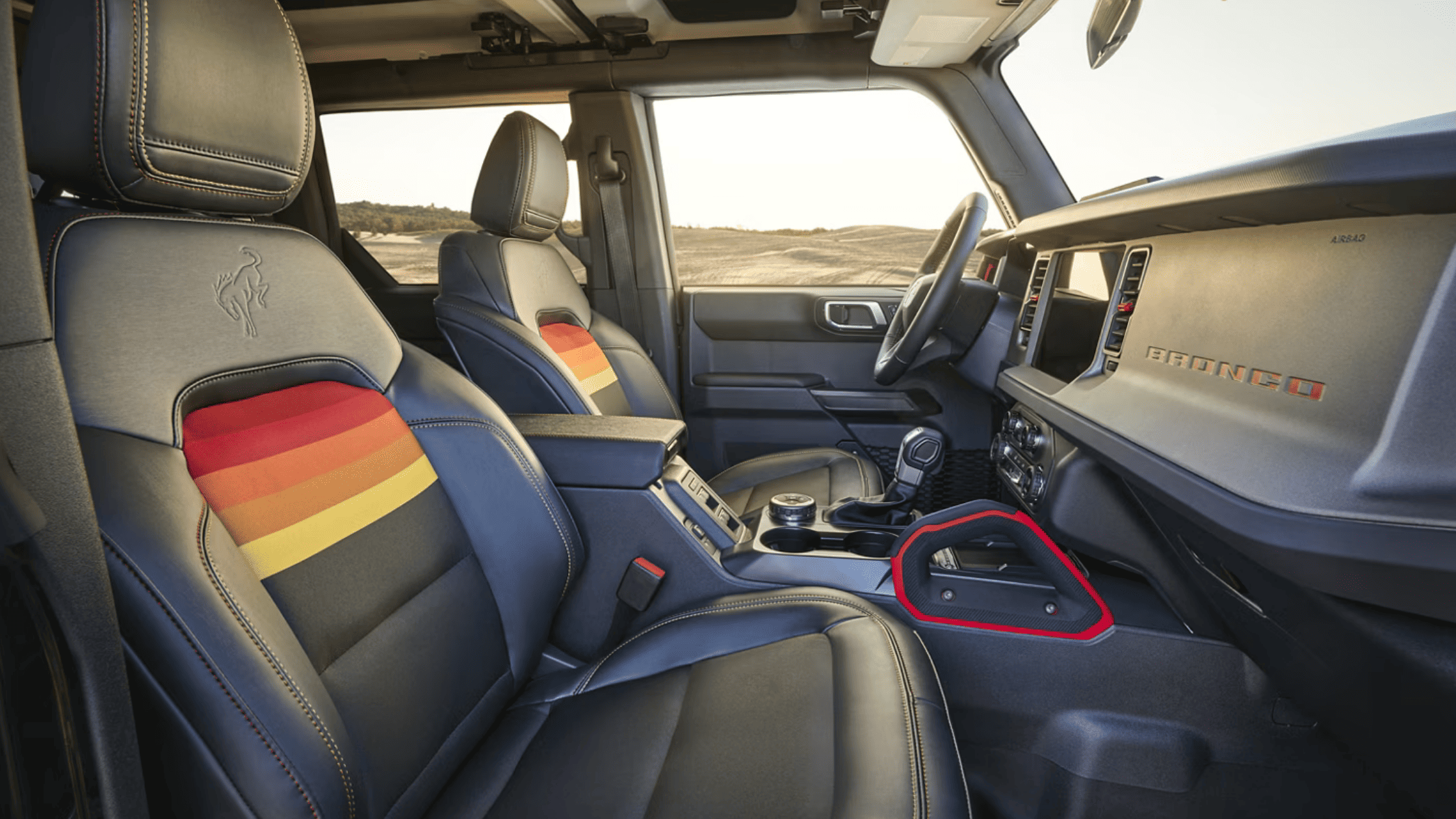 Interior view of the 2025 Ford Bronco® in Cleveland, OH, featuring leather seats with a distinctive multicolor stripe on the driver's seat, showcasing the iconic Bronco logo. The dashboard displays modern controls and the Bronco branding, highlighting a spacious and well-equipped cabin.