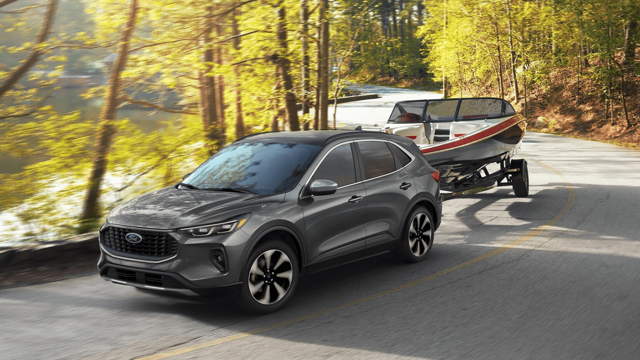 In Cleveland, OH, the 2025 Ford Escape® confidently tows a boat along a forested road beside a serene lake.