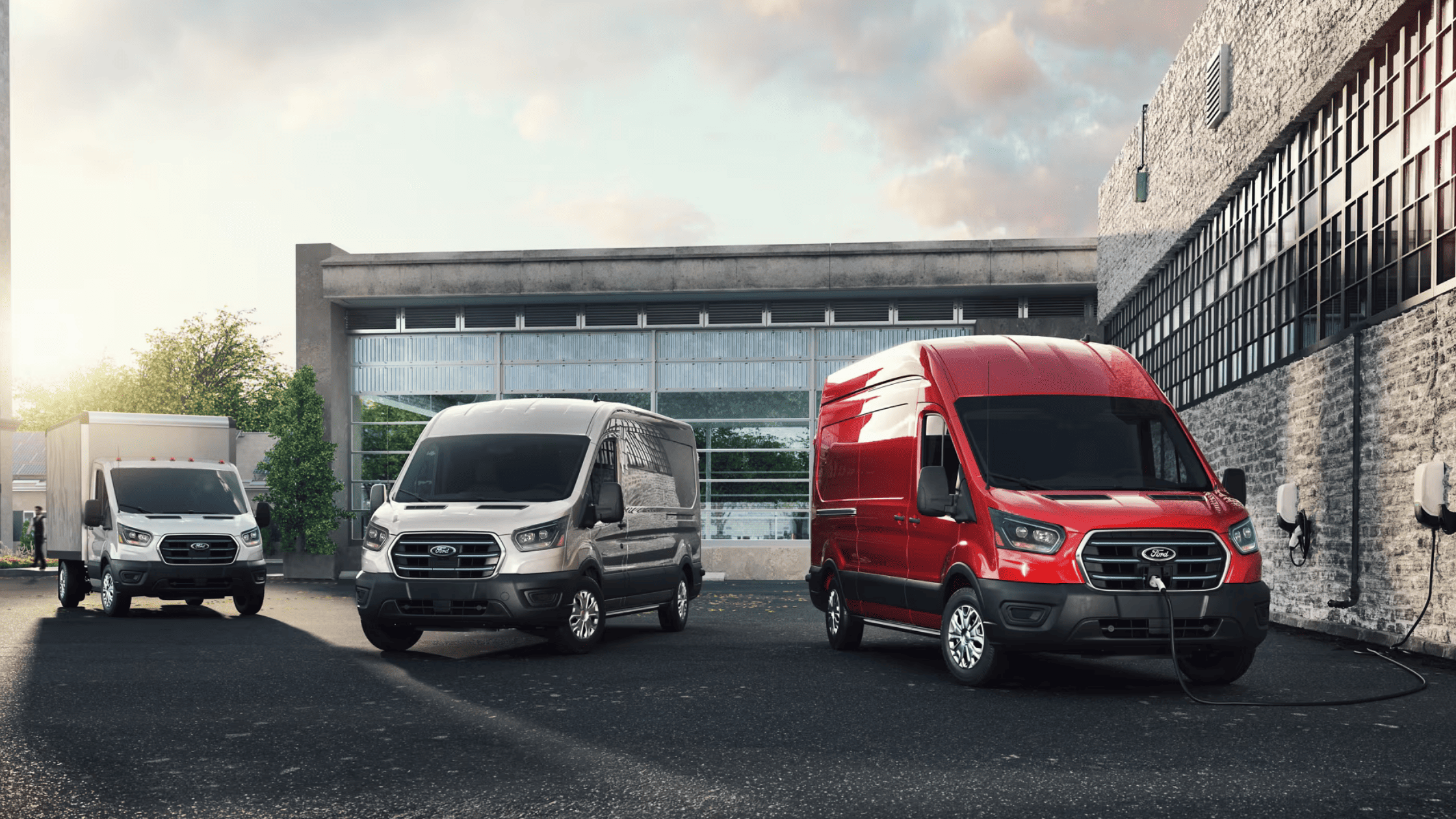 Lineup of 2025 Ford E-Transit vans charging outside a commercial building in Cleveland, OH