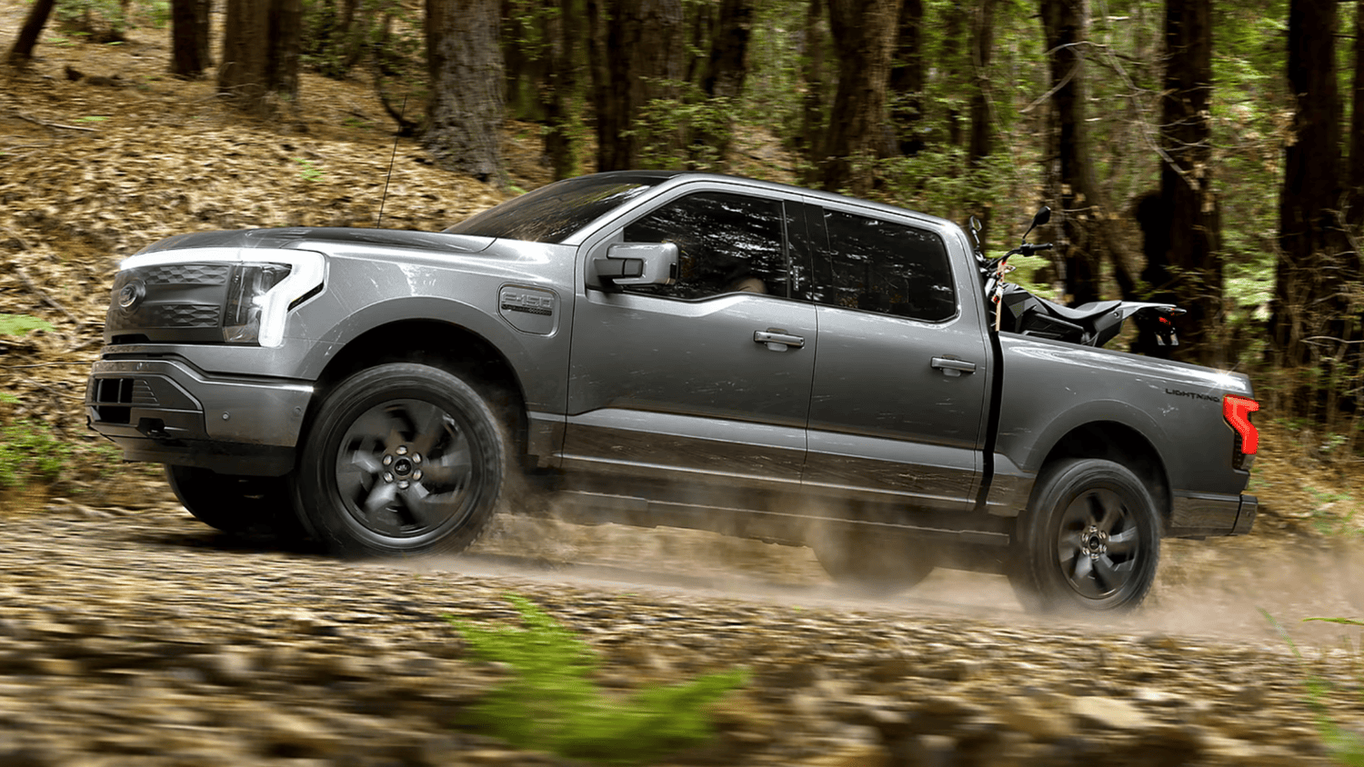2024 Ford F-150® Lightning driving off-road through wooded trails near Euclid, OH, emphasizing its rugged electric truck capability.https://www.nickmayerfordwest.com/searchnew.aspx?q=2024%20Ford%20F-150%20Lightning